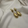 Gold-tone teardrop dangle earrings on white fabric background