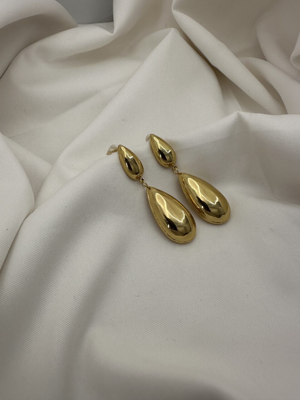 Gold-tone teardrop dangle earrings on white fabric background